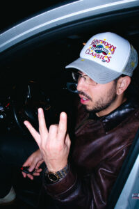 Young man in baseball cap and rectangle metal rim glasses poses in car.