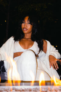 Young woman poses by the fireside in a fuzzy three piece white set.