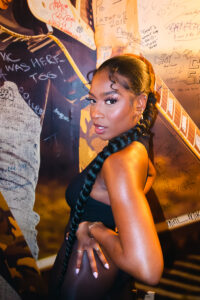 Young woman with a single long braid poses while slightly looking back at the camera.