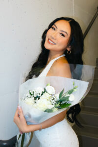 Young woman in white dress with decorative pearls poses with assorted white flower bouquet.